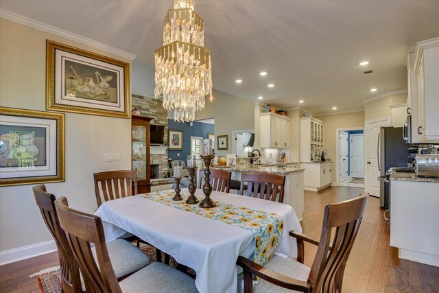 dining space with sink, ornamental molding, a fireplace, a notable chandelier, and dark hardwood / wood-style flooring