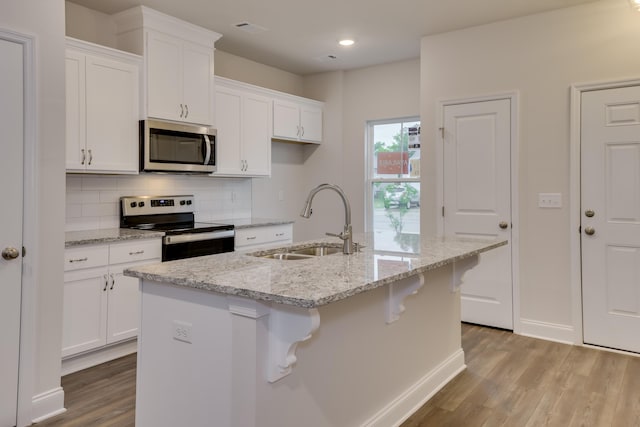 kitchen featuring decorative backsplash, appliances with stainless steel finishes, sink, white cabinets, and an island with sink