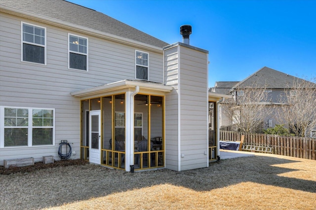 back of property with a chimney, fence, roof with shingles, and a sunroom