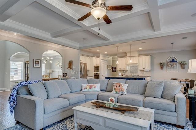 living area with beamed ceiling, arched walkways, coffered ceiling, and wood finished floors