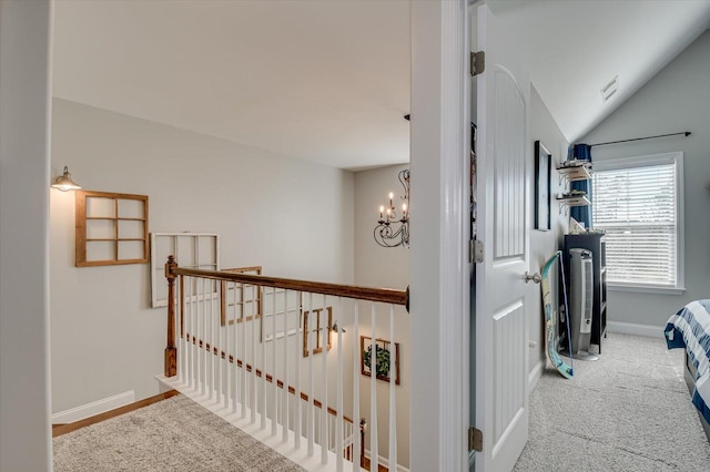 hall featuring carpet, baseboards, an inviting chandelier, vaulted ceiling, and an upstairs landing