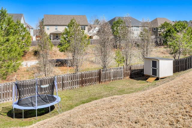 view of yard with a fenced backyard, a trampoline, an outdoor structure, and a storage shed