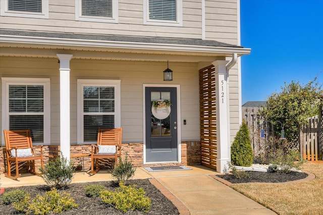 entrance to property featuring fence, covered porch, and stone siding