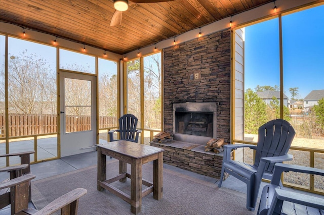 sunroom featuring ceiling fan, wooden ceiling, track lighting, and an outdoor stone fireplace