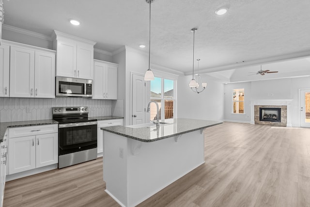 kitchen featuring white cabinetry, a kitchen island with sink, stainless steel appliances, ornamental molding, and decorative light fixtures