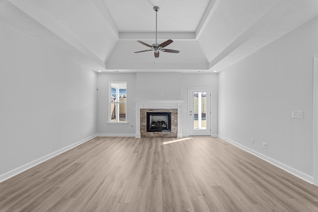 unfurnished living room featuring a stone fireplace, a wealth of natural light, and a raised ceiling