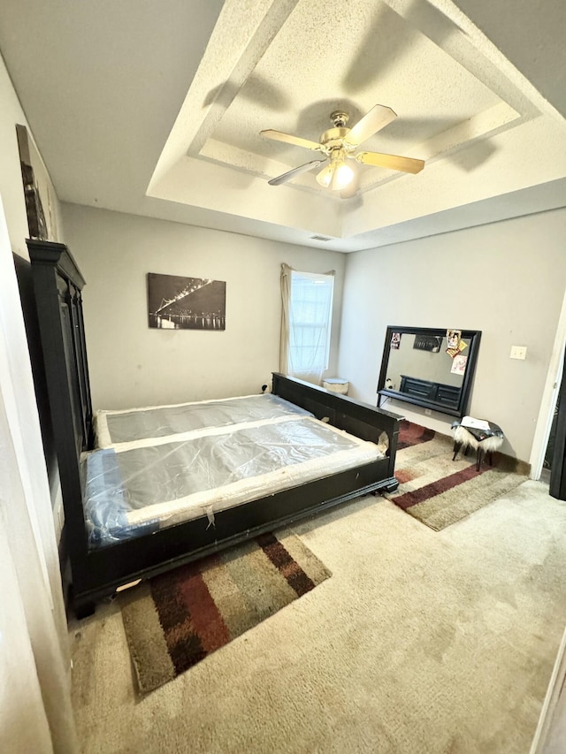 bedroom featuring ceiling fan, carpet floors, a textured ceiling, and a tray ceiling