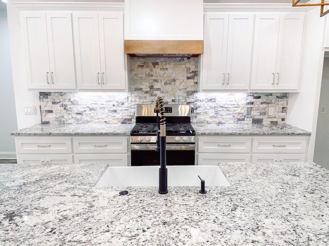 kitchen featuring light stone counters, stainless steel range with gas cooktop, white cabinetry, and decorative backsplash