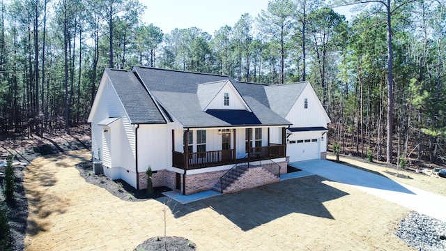 modern farmhouse featuring central AC unit, an attached garage, covered porch, a shingled roof, and concrete driveway