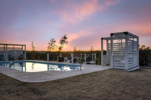 pool at dusk with a patio area and a lawn