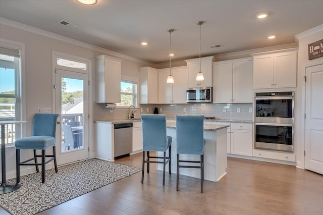 kitchen featuring white cabinets, a kitchen island, stainless steel appliances, and decorative light fixtures