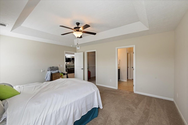 carpeted bedroom with a walk in closet, a textured ceiling, a raised ceiling, and baseboards