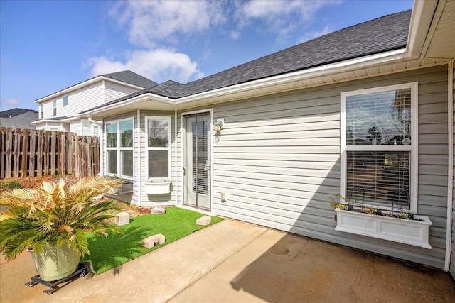 property entrance with a shingled roof, a patio, and fence