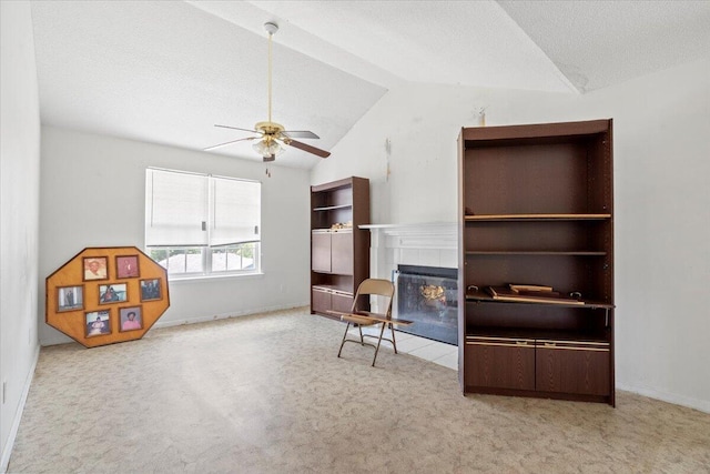 living area featuring ceiling fan, a textured ceiling, lofted ceiling, a tiled fireplace, and light carpet