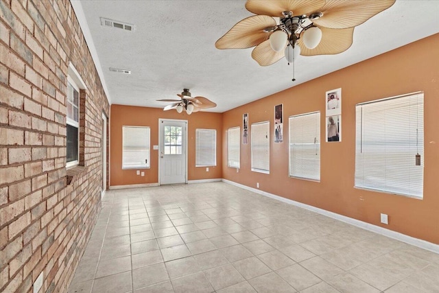 tiled spare room featuring a textured ceiling and brick wall