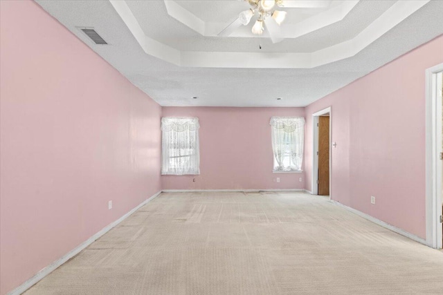 unfurnished room featuring a textured ceiling, ceiling fan, a raised ceiling, and light carpet