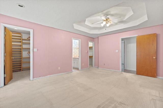 unfurnished bedroom with connected bathroom, a spacious closet, ceiling fan, a tray ceiling, and a closet