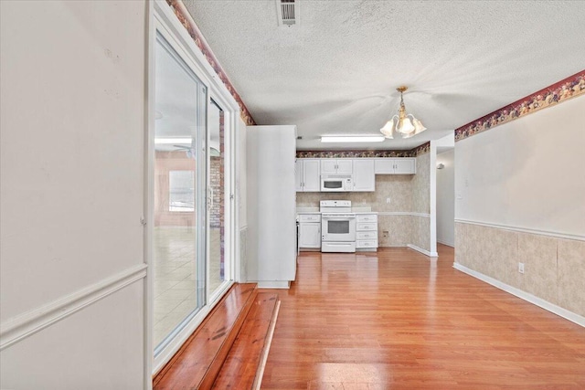 kitchen with pendant lighting, white appliances, white cabinets, light wood-type flooring, and a chandelier