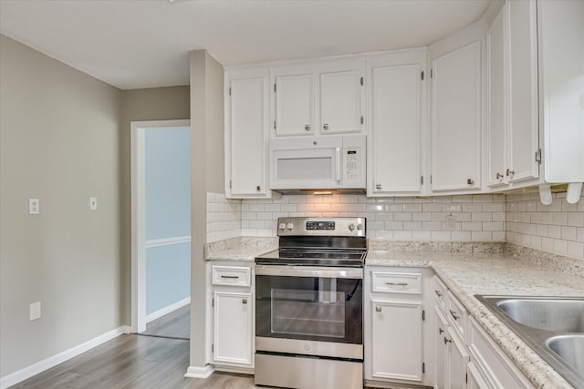 kitchen with stainless steel range with electric stovetop, white microwave, decorative backsplash, and white cabinetry