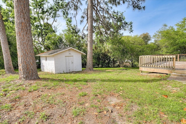 view of grassy yard with a storage unit, an outbuilding, a deck, and view of wooded area
