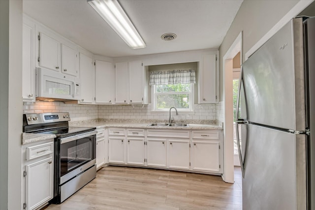 kitchen with stainless steel appliances, a sink, white cabinetry, light wood finished floors, and light countertops