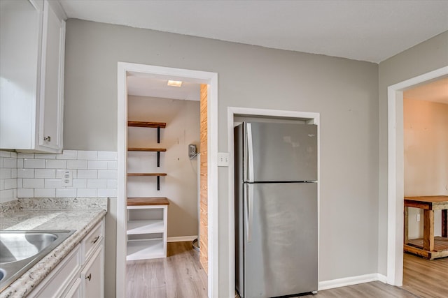 kitchen featuring freestanding refrigerator, light wood-type flooring, white cabinetry, and decorative backsplash