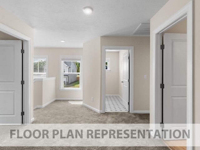 hall with a textured ceiling, carpet flooring, visible vents, and baseboards