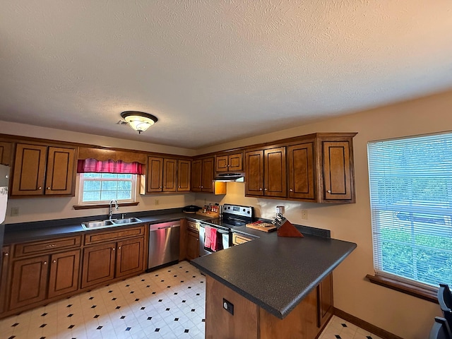 kitchen with under cabinet range hood, dark countertops, appliances with stainless steel finishes, and a sink
