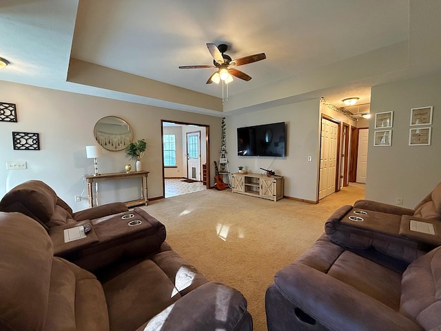 living room featuring baseboards, a ceiling fan, a raised ceiling, and light carpet