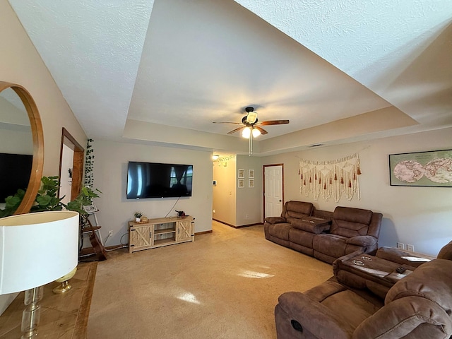 living area featuring baseboards, a ceiling fan, light carpet, and a tray ceiling