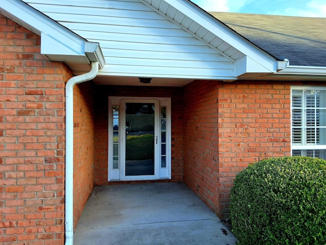 view of exterior entry with brick siding and a shingled roof