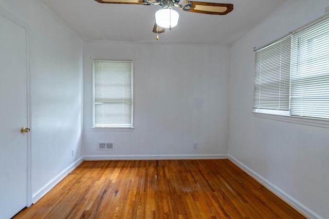 empty room with a wealth of natural light, hardwood / wood-style flooring, ceiling fan, and ornamental molding