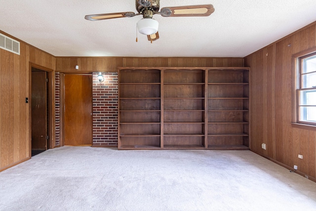 carpeted empty room with ceiling fan, wood walls, and a textured ceiling