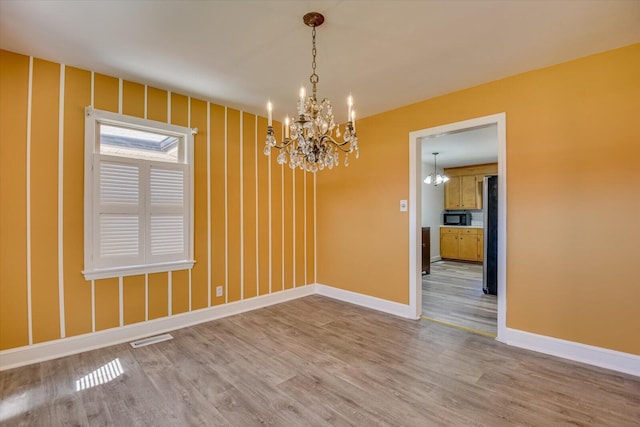 unfurnished dining area featuring a notable chandelier, visible vents, baseboards, and wood finished floors