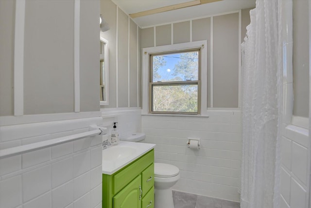 bathroom with tile walls, toilet, wainscoting, tile patterned floors, and vanity