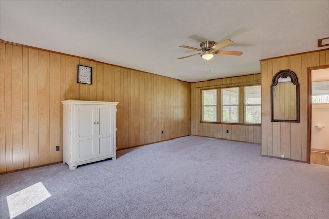 empty room featuring wooden walls, carpet, baseboards, and ceiling fan