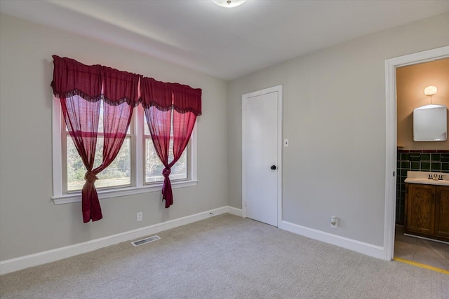 unfurnished bedroom with a sink, visible vents, light carpet, and baseboards