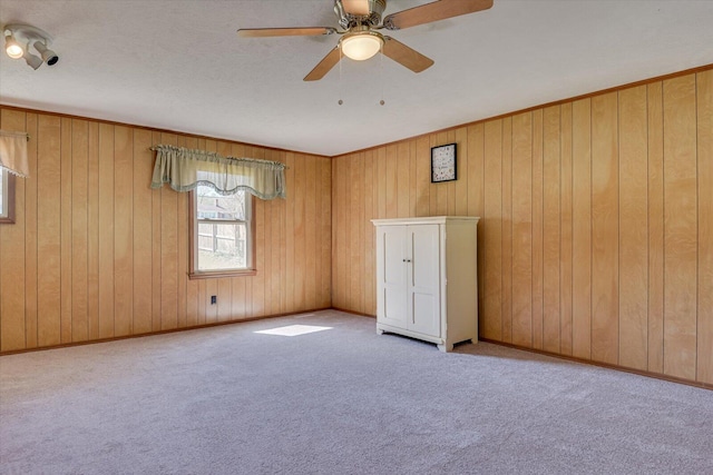 unfurnished room featuring baseboards, carpet, ceiling fan, and wooden walls