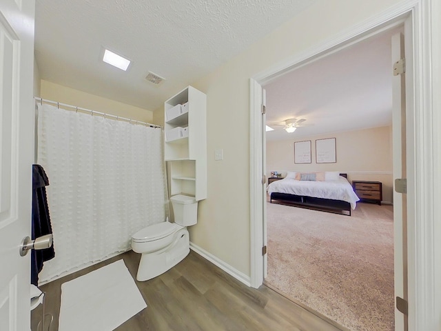 ensuite bathroom with a textured ceiling, toilet, wood finished floors, baseboards, and a shower with curtain