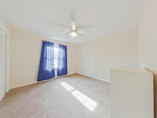 carpeted empty room with a ceiling fan and baseboards