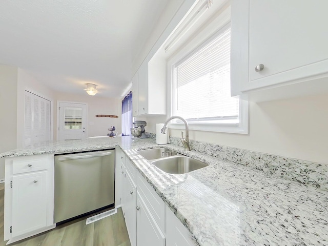 kitchen with white cabinets, light wood-style flooring, a peninsula, stainless steel dishwasher, and a sink