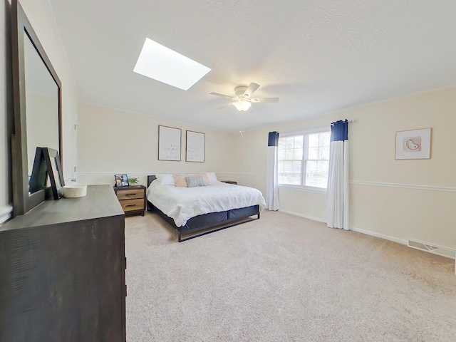 bedroom featuring light carpet, a skylight, baseboards, ceiling fan, and a textured ceiling