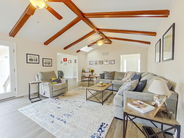 living area featuring lofted ceiling with skylight, wood finished floors, visible vents, and a ceiling fan