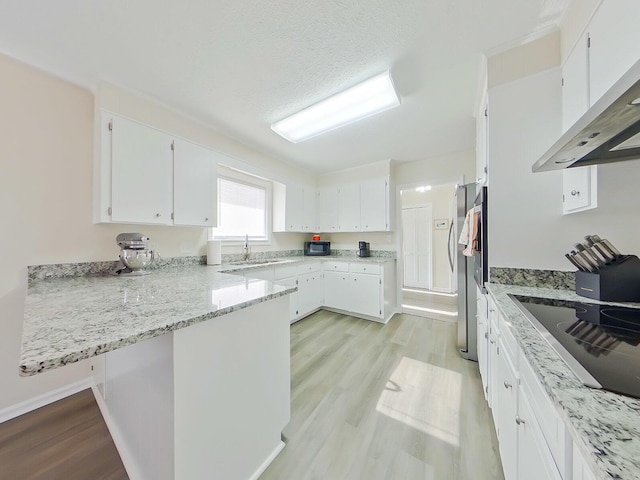 kitchen featuring a peninsula, a sink, exhaust hood, white cabinetry, and light wood-type flooring