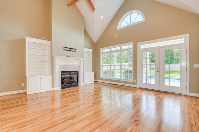 unfurnished living room with high vaulted ceiling, wood finished floors, ceiling fan, a tiled fireplace, and baseboards
