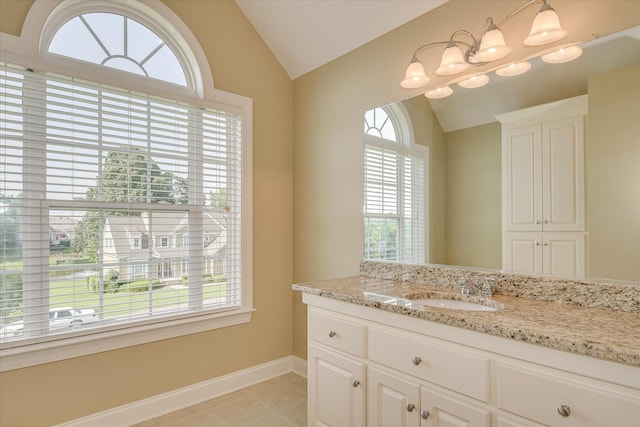 bathroom with vaulted ceiling, healthy amount of natural light, baseboards, vanity, and tile patterned flooring
