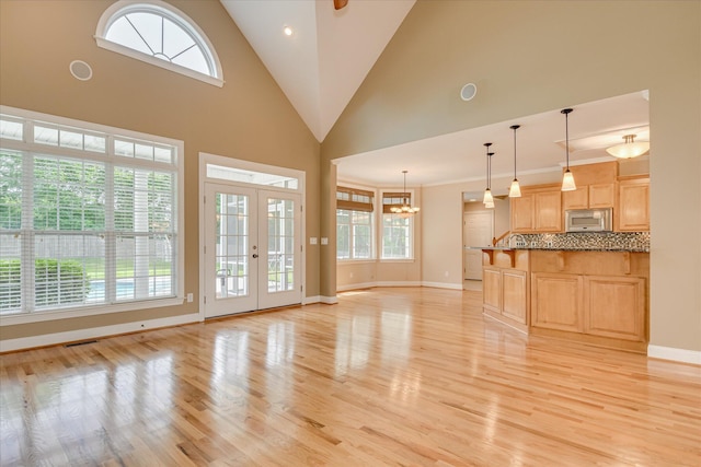 unfurnished living room with healthy amount of natural light, light wood-type flooring, baseboards, and high vaulted ceiling