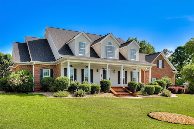 cape cod house with brick siding, a front yard, a porch, a shingled roof, and stucco siding