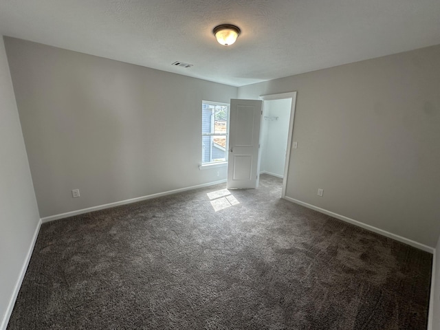 empty room with visible vents, baseboards, dark carpet, and a textured ceiling
