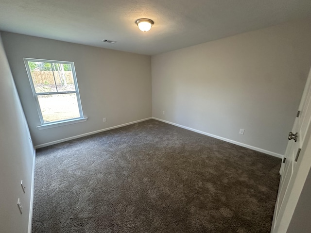 unfurnished room with baseboards, dark carpet, and visible vents
